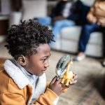 A child uses a magnifying glass to study a small plastic dinosaur figure.